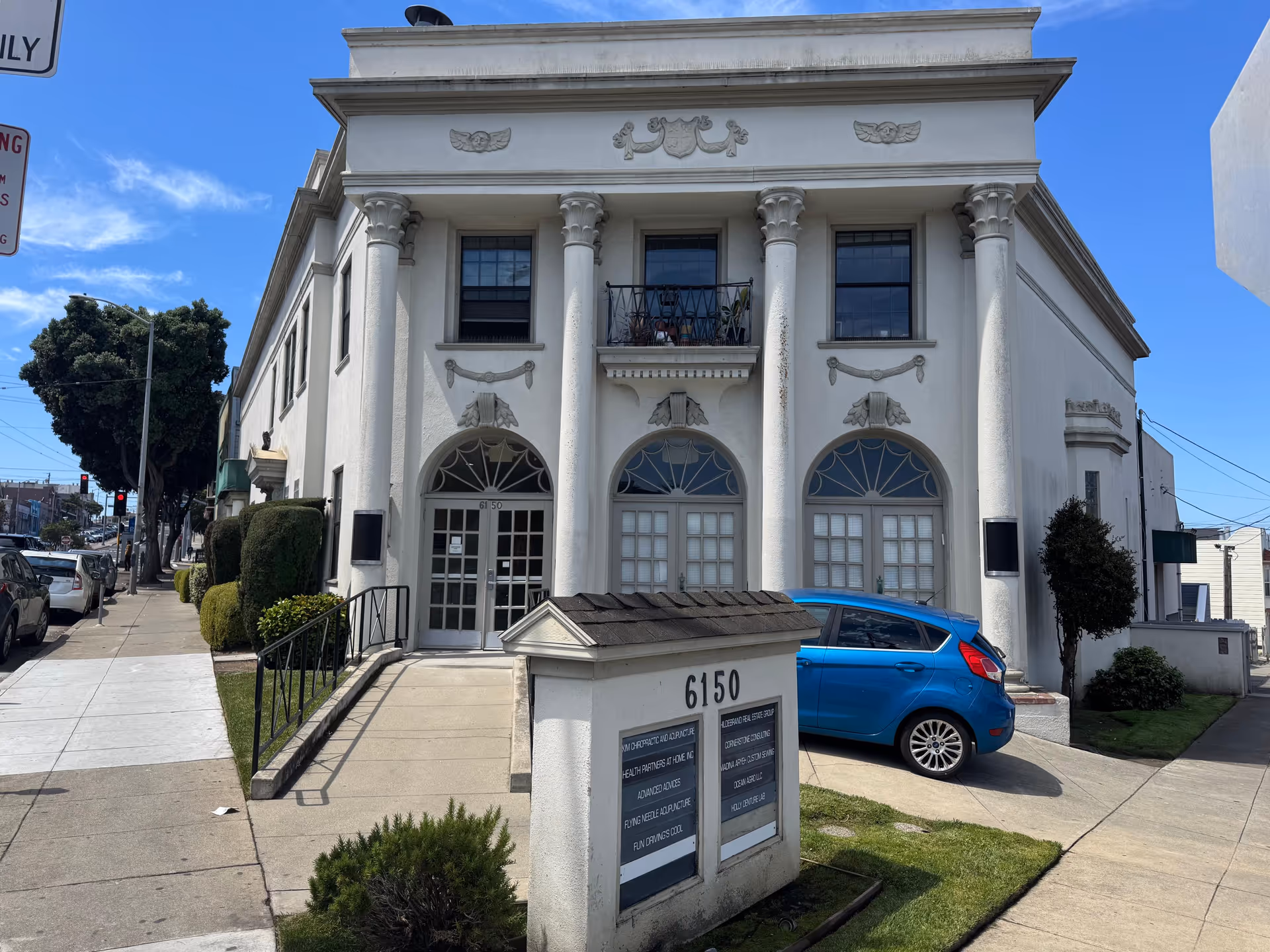 White classical building with tall columns and arched windows on a sunny street.