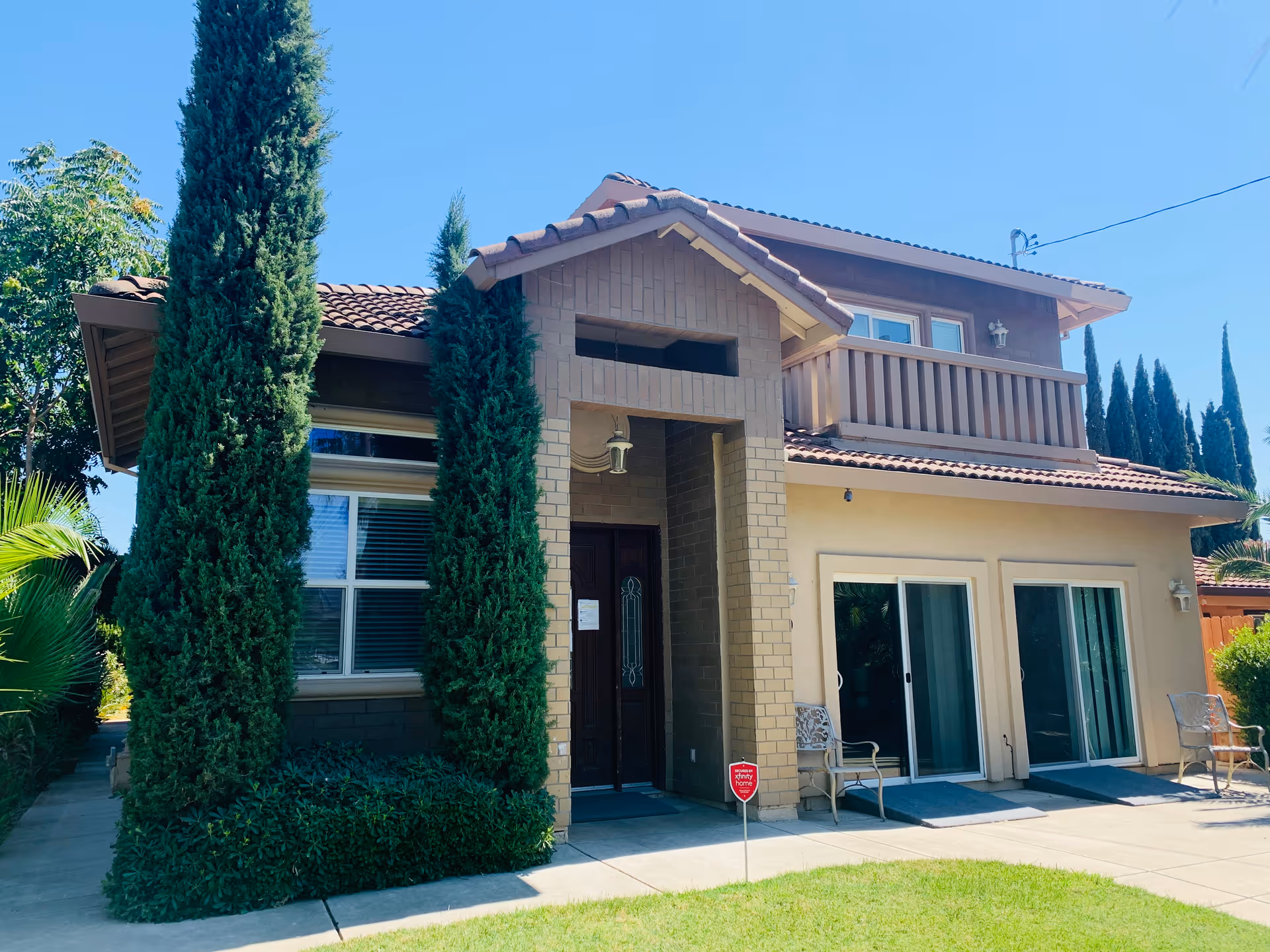 Two-story house with a covered entrance, balcony, and tall evergreen trees in front yard.