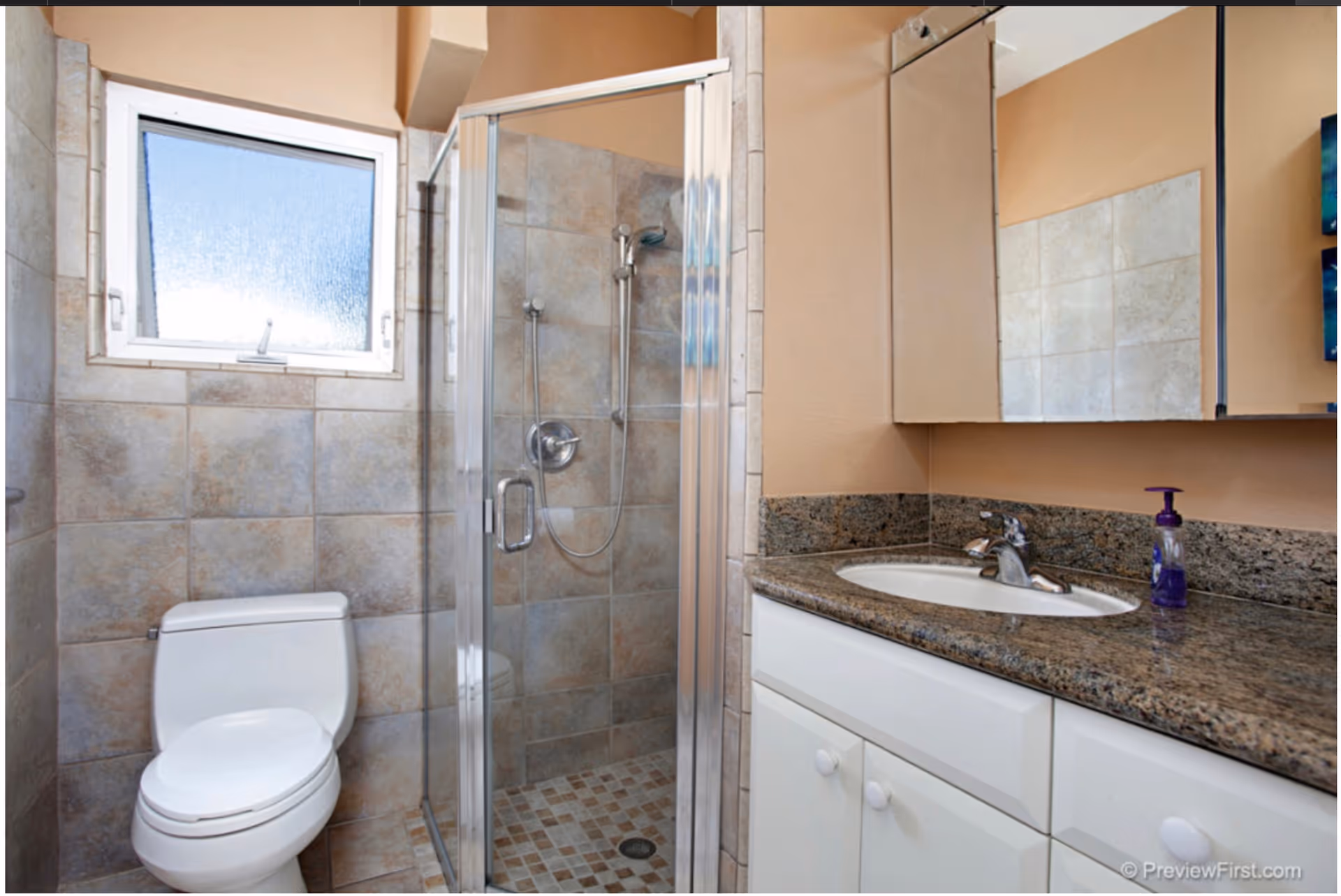 Tiled bathroom featuring a shower stall, toilet, and granite counter with sink.