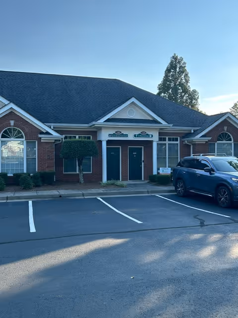 Brick senior living facility entrance with signage, shrubs, and a blue car in the parking lot.
