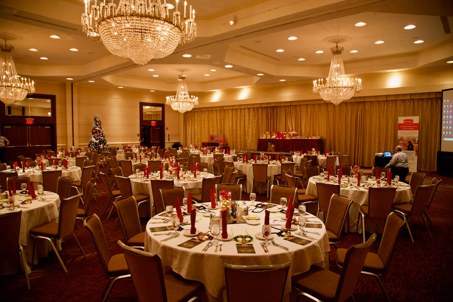 Spacious banquet hall interior with round tables, chandeliers, and festive decor.