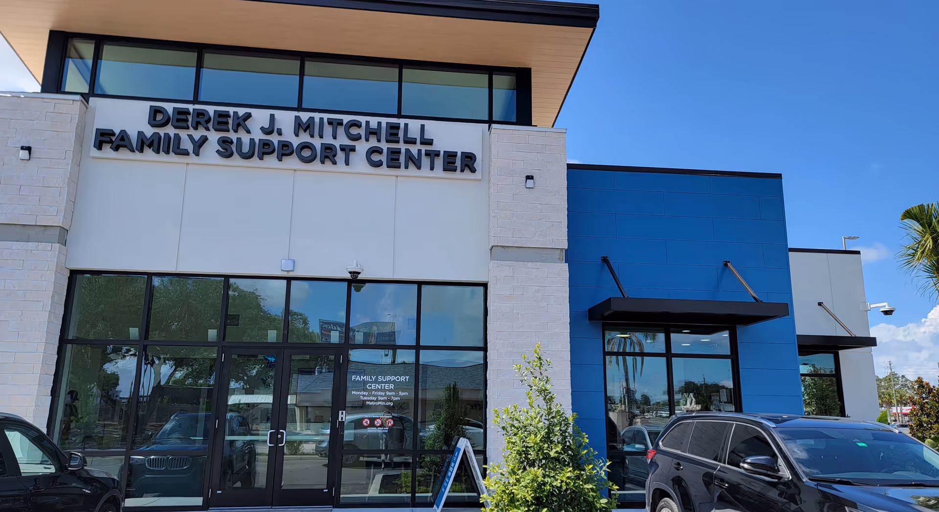 Front view of Derek J. Mitchell Family Support Center with glass doors and blue exterior panels.