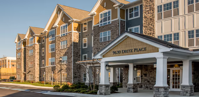 Exterior view of a multi-story senior living facility with stone facade and covered entrance.