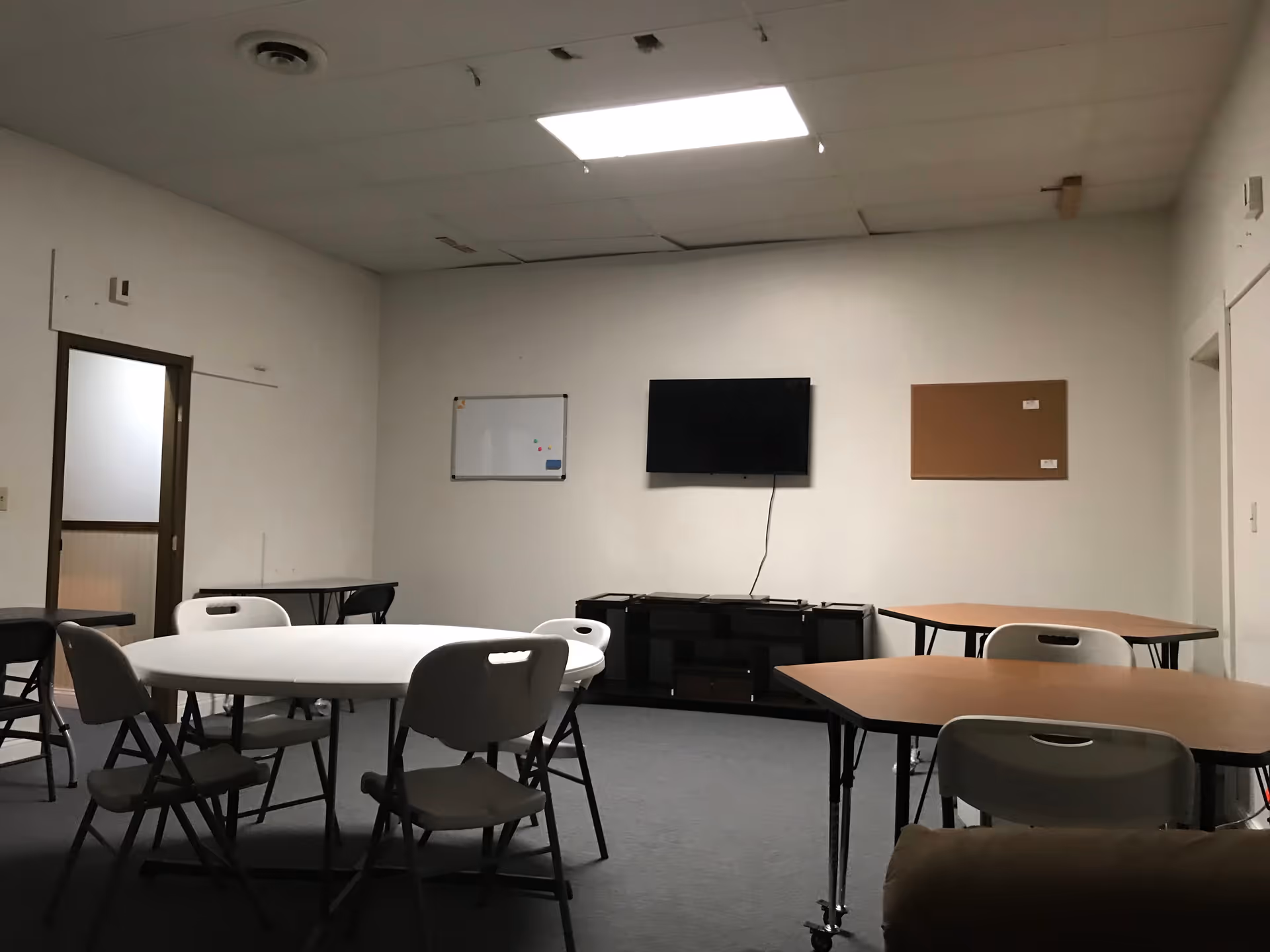 Empty multipurpose room with round tables, chairs, and a wall-mounted TV.