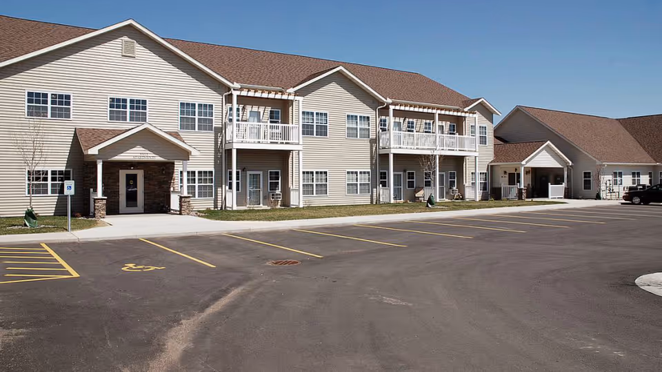 Exterior view of Good Care senior living facility with parking lot and balconies.