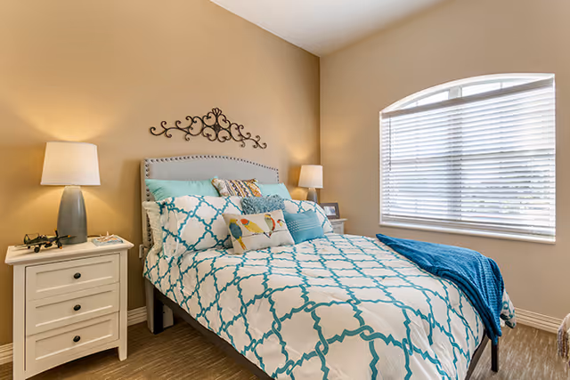 Cozy senior living bedroom with a patterned bedspread, two lamps, and an arched window.