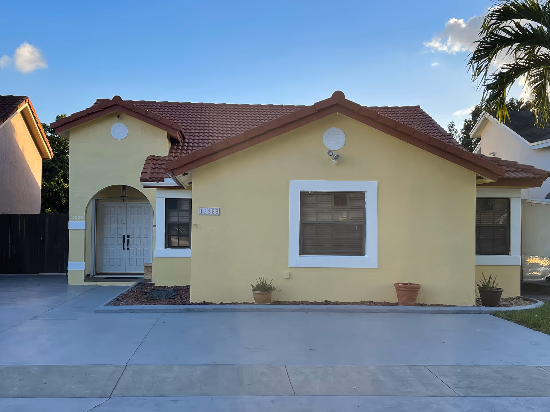 Yellow single-story building with red-tiled roof and driveway in front of Kendall Haven ALF
