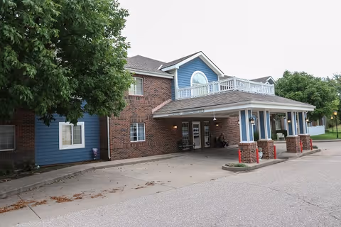 Brick and blue senior living building exterior with a covered entrance and seating.