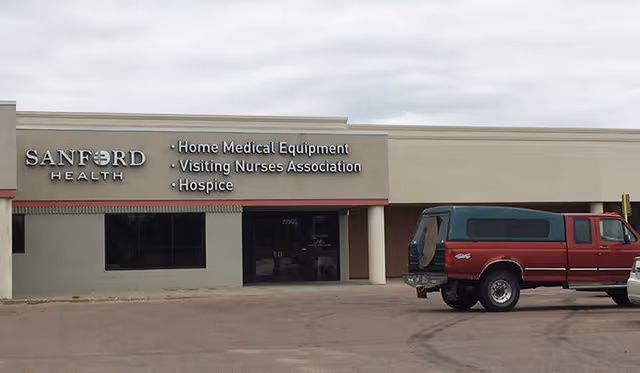 Exterior view of Sanford Health facility with signage and a red van parked in front.