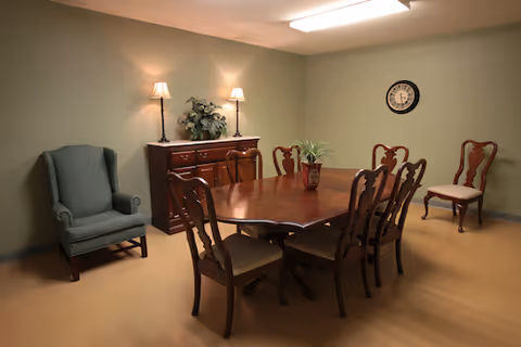 Formal dining room with wooden table, chairs, sideboard, clock, and plants.