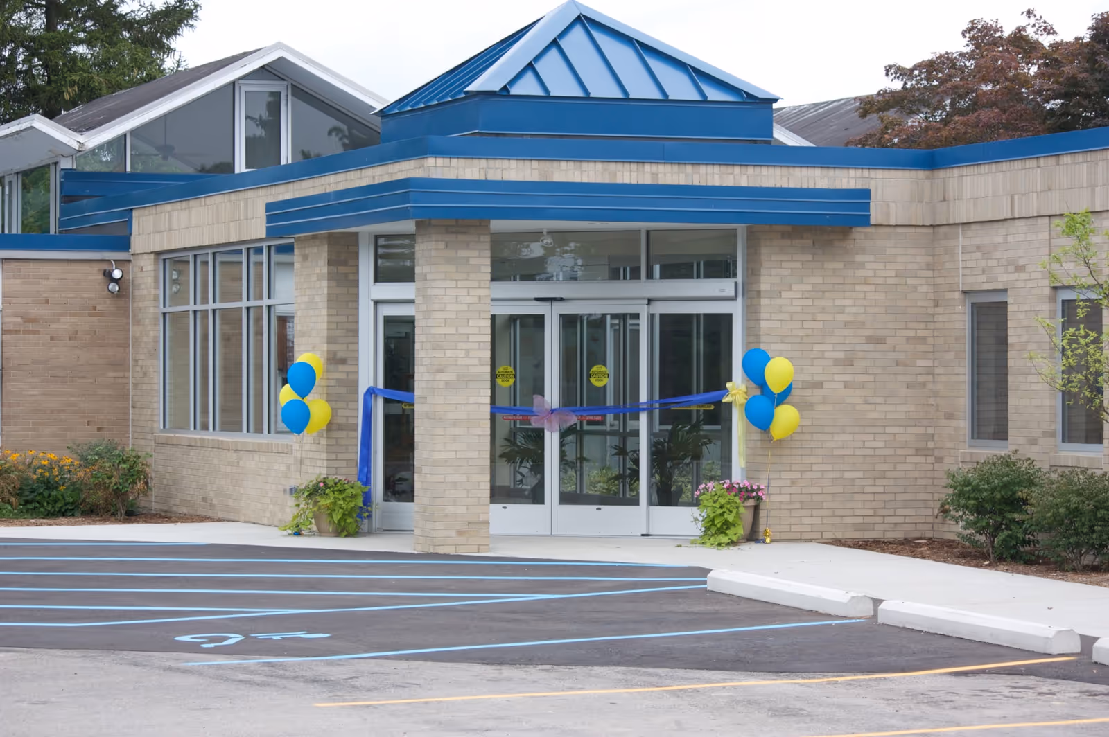 Exterior view of the building entrance with glass doors, blue trim, and balloons.