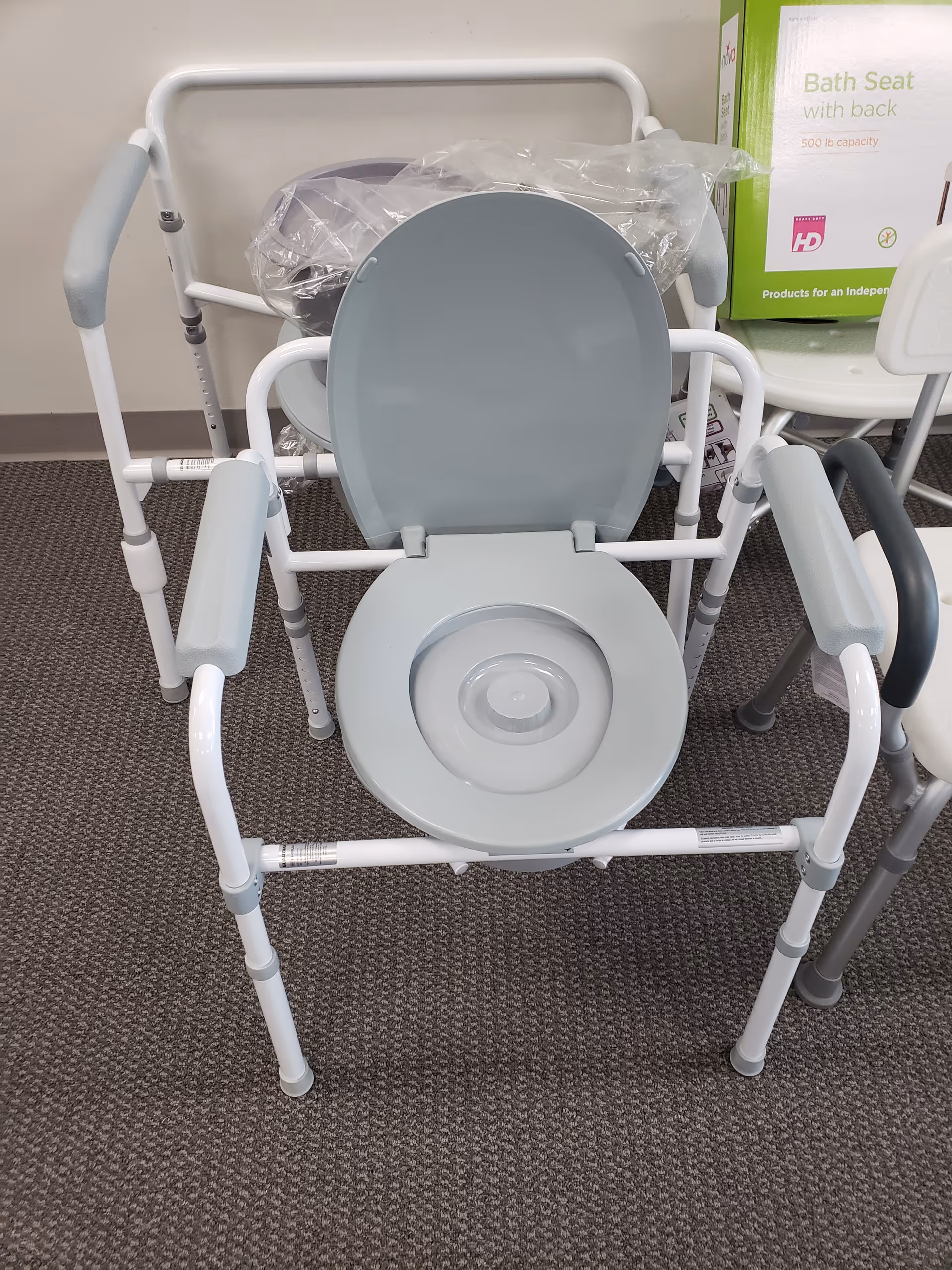 Gray upright commode chair with backrest in a senior care facility room.