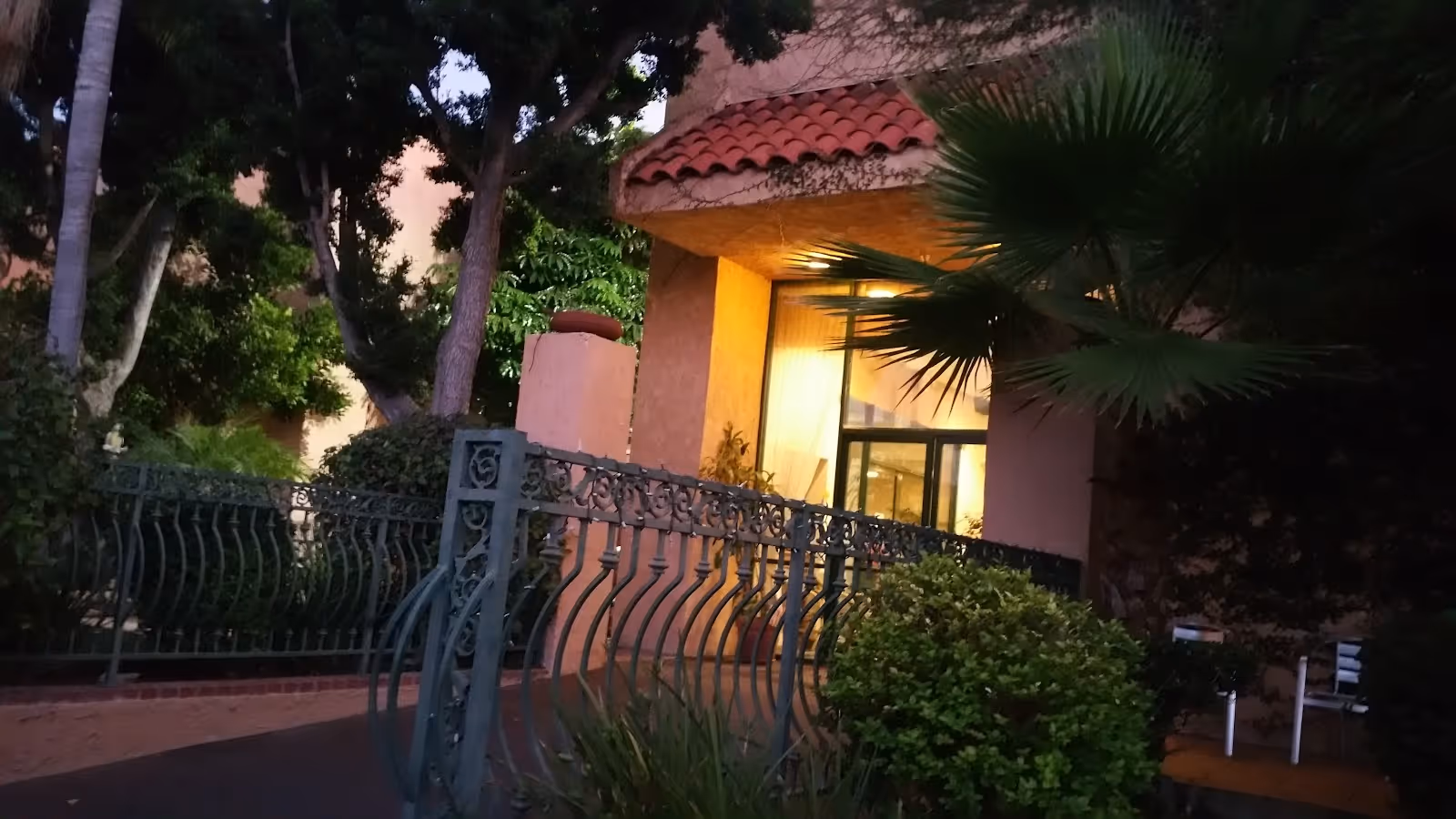 Evening exterior of Palos Verdes Villa entrance with wrought-iron railing and surrounding shrubbery.