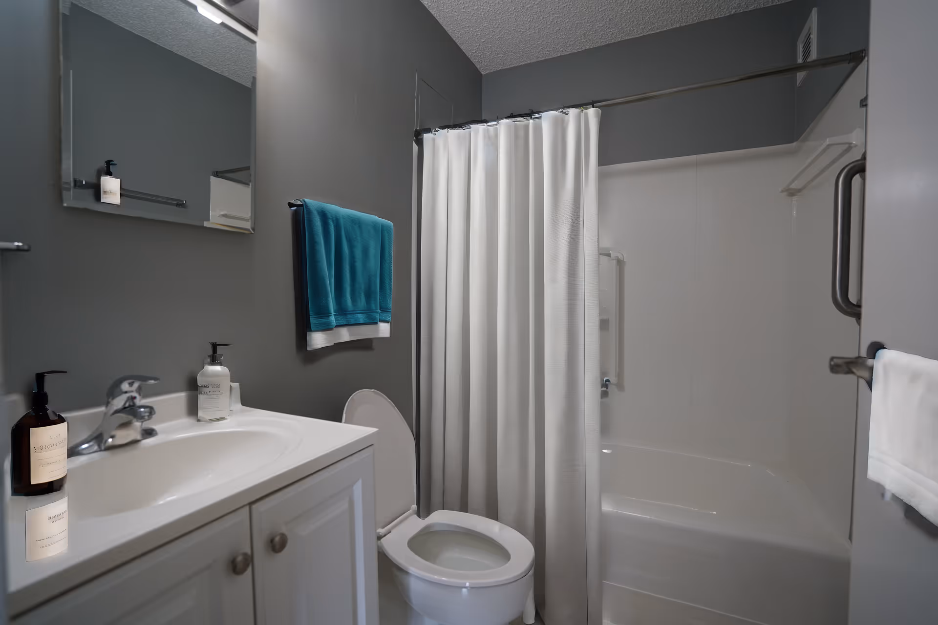 Modern bathroom with sink, toilet, shower, and white curtain against gray walls.
