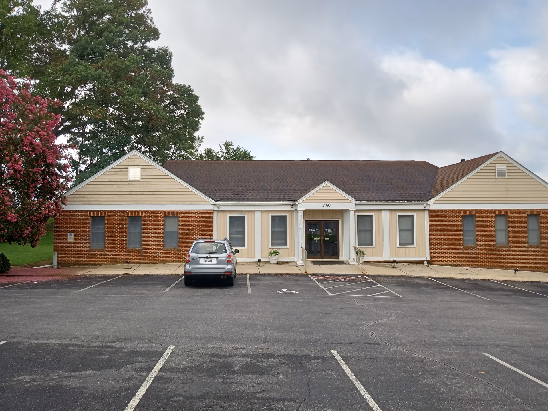 Single-story facility with brick and beige siding, glass doors, and a parking lot in front.