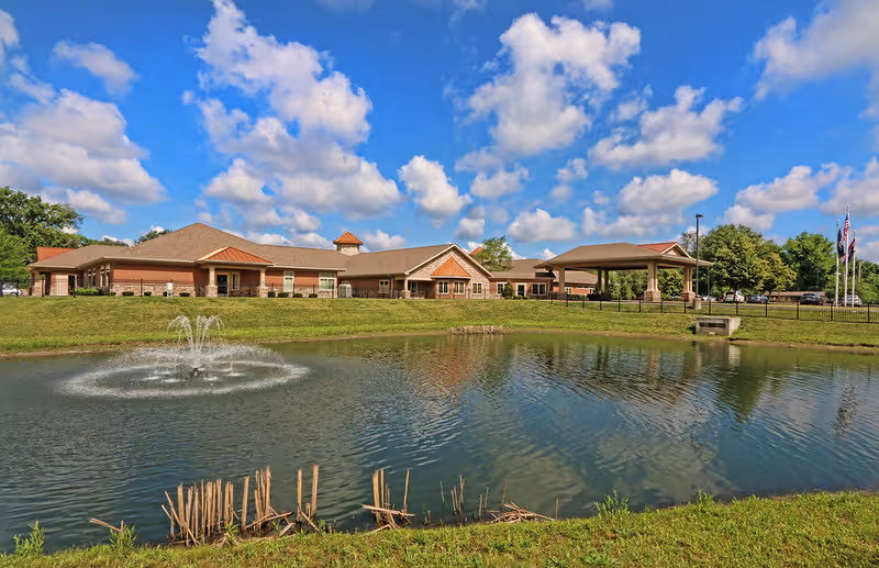 Exterior view of Life Care Center of Florissant with pond, fountain, and clear blue sky.