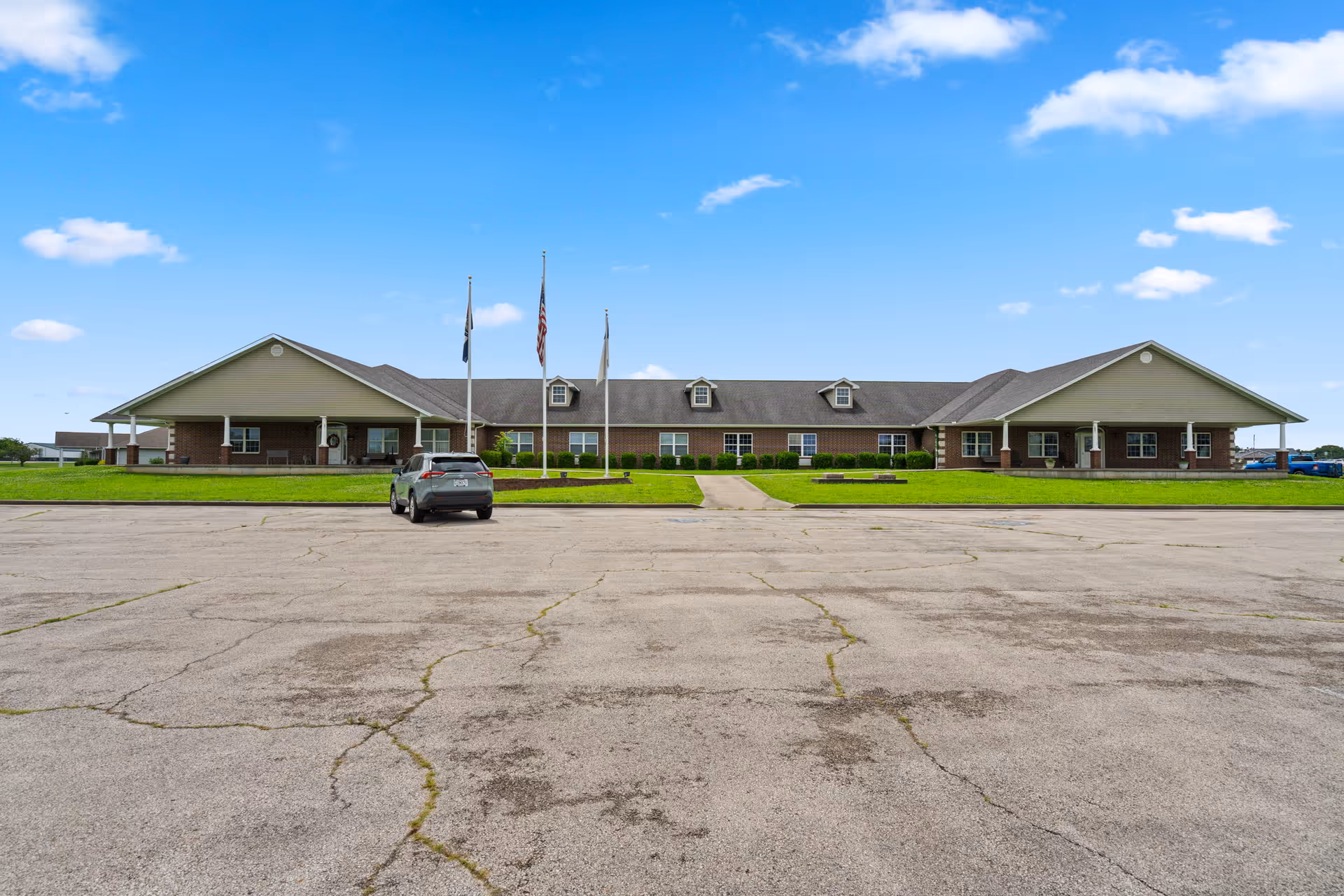 Wide, single-story care home building with flagpoles and a parked car in front.