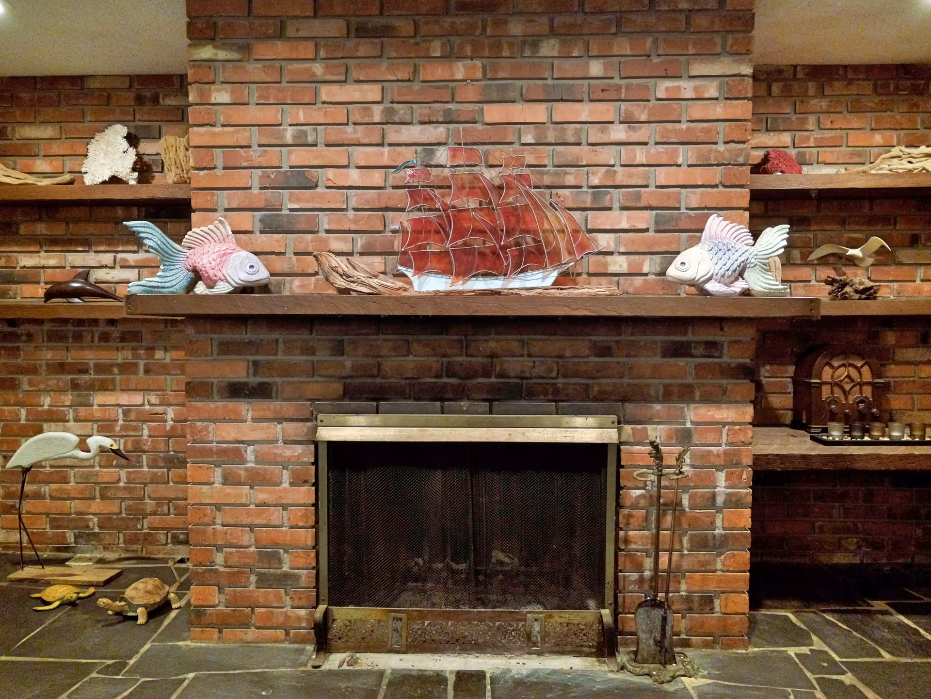Brick fireplace with a wooden mantel displaying nautical decor including two ceramic fish and a stained-glass ship sculpture.