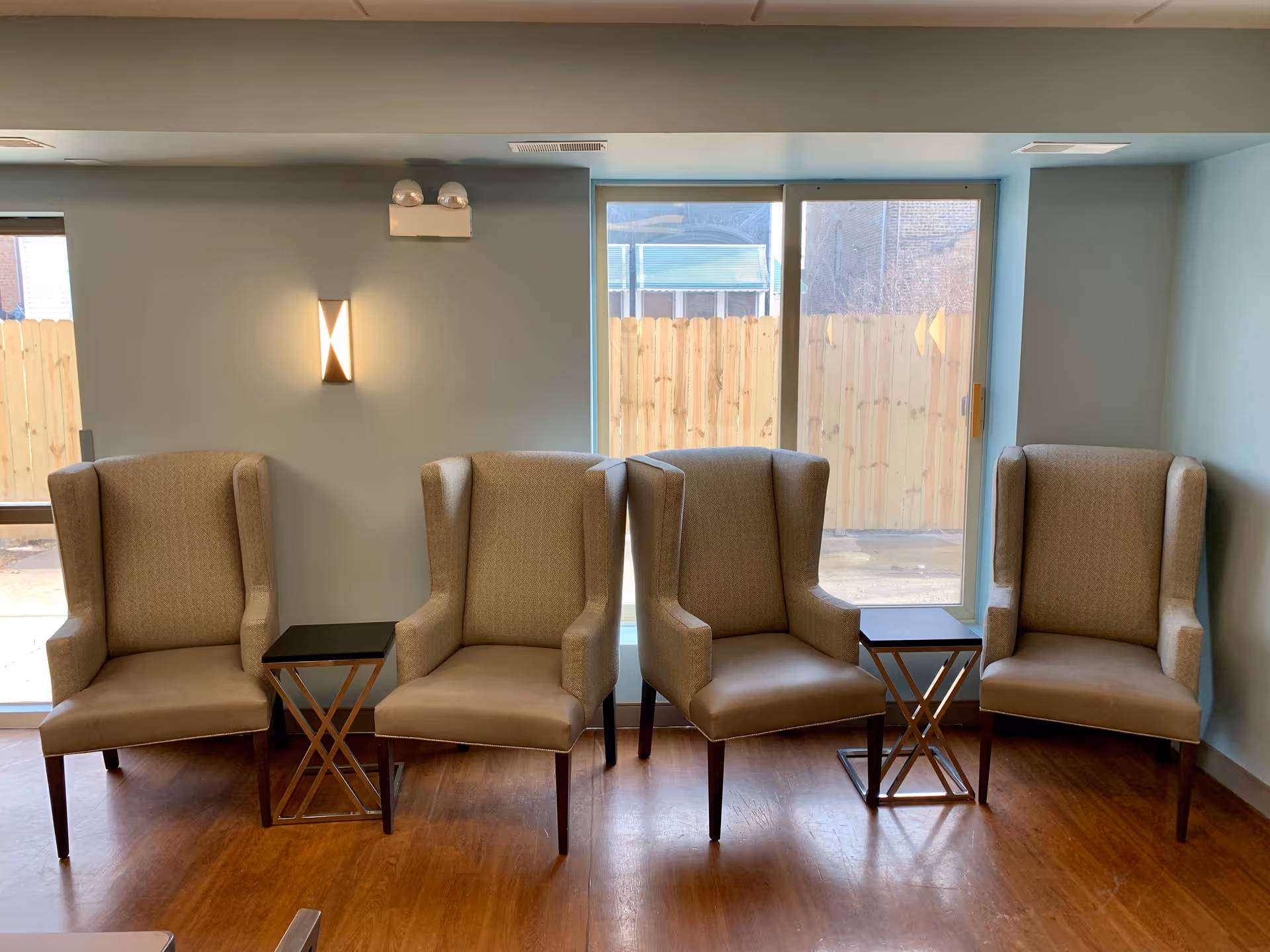 A row of beige high-back chairs with small side tables in a light blue lounge.