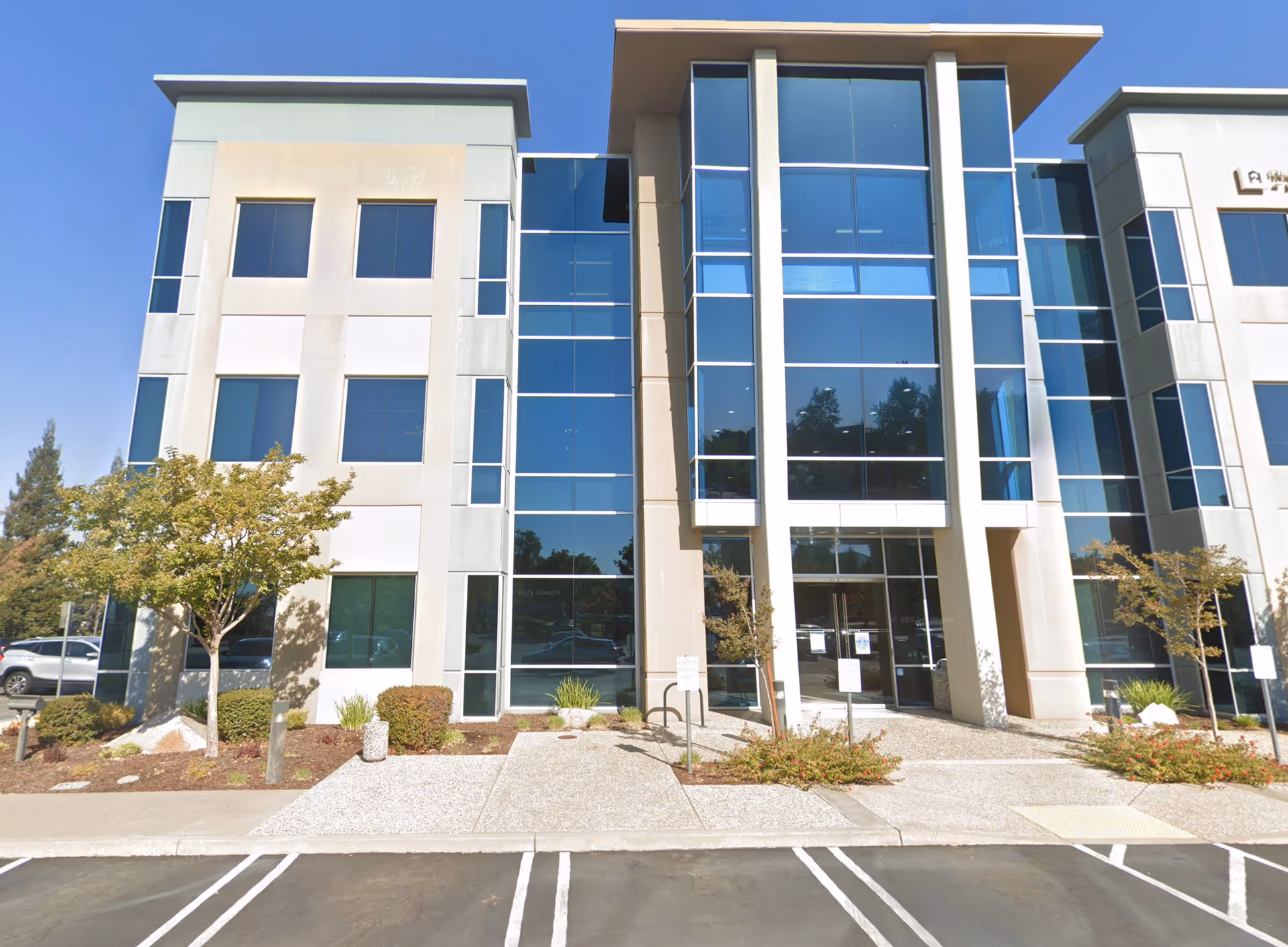 Modern glass-front senior care building with landscaping and parking in daylight.