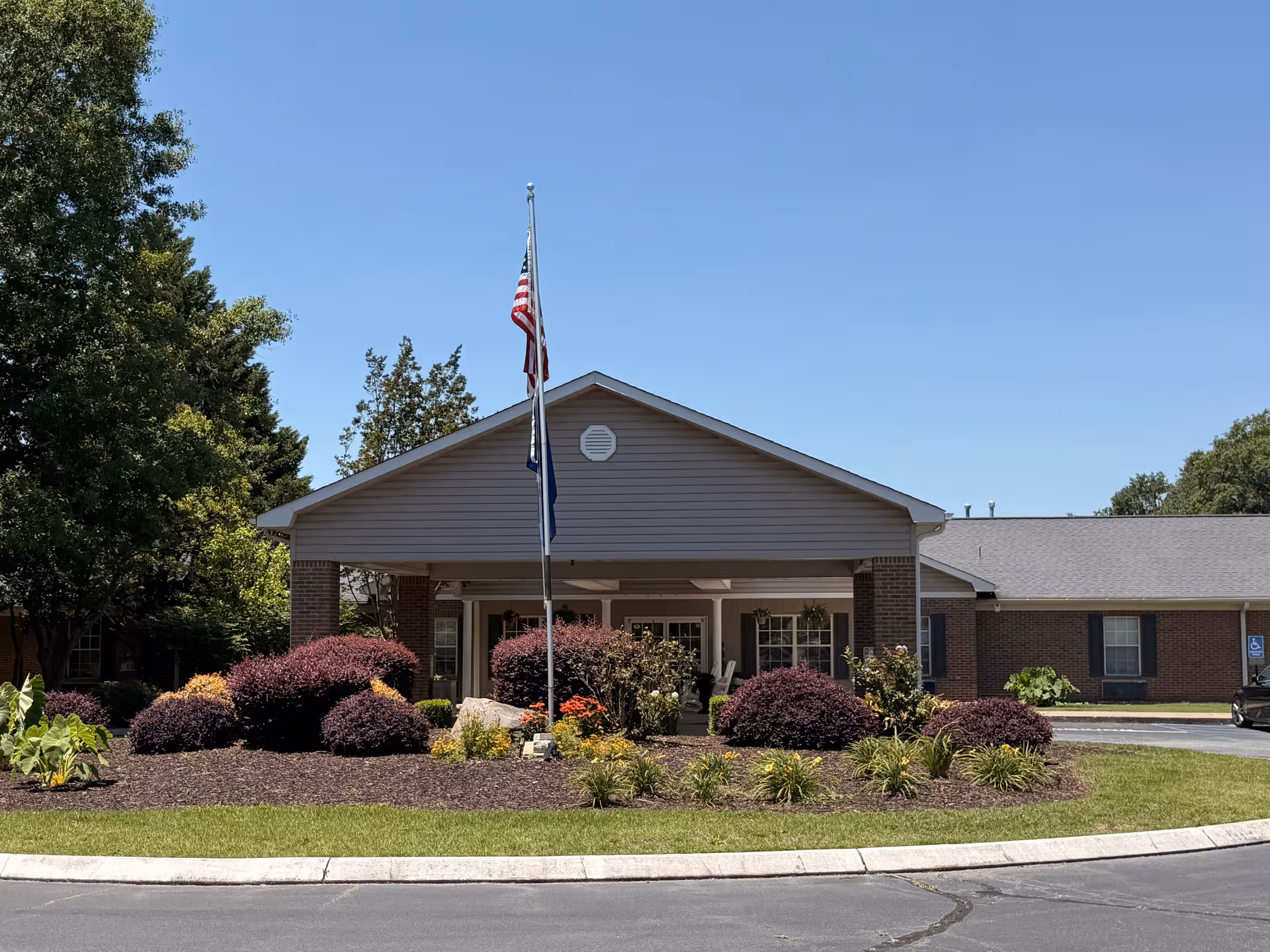 Senior living facility entrance with flagpole, shrubs, and brick facade.