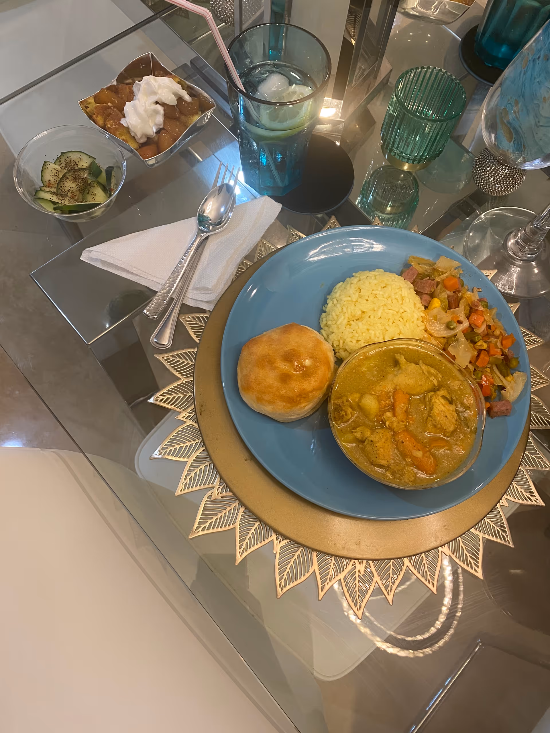 Meal served on glass dining table with rice, curry, bread roll, and vegetables.