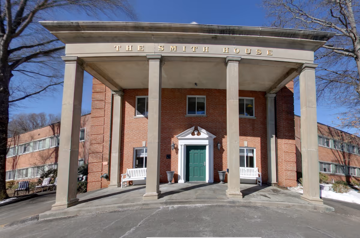 Brick building with large columns, a green door, and white benches at the entrance.