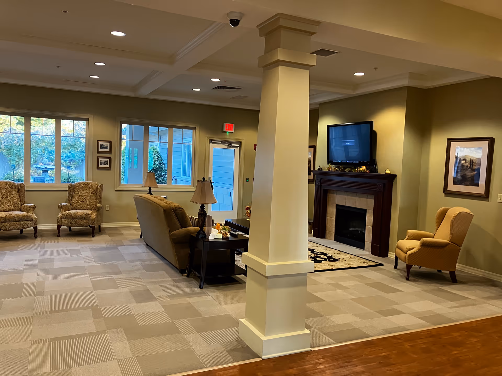 Spacious senior living lounge with seating, a fireplace, TV, and decorative columns.