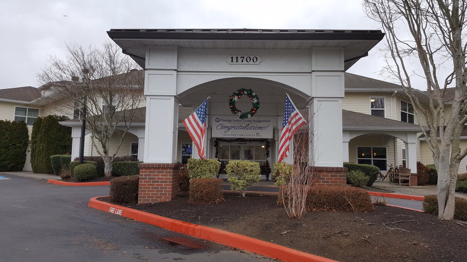 Front entrance of Prestige Senior Living Bridgewood with arches, wreath, and flags.