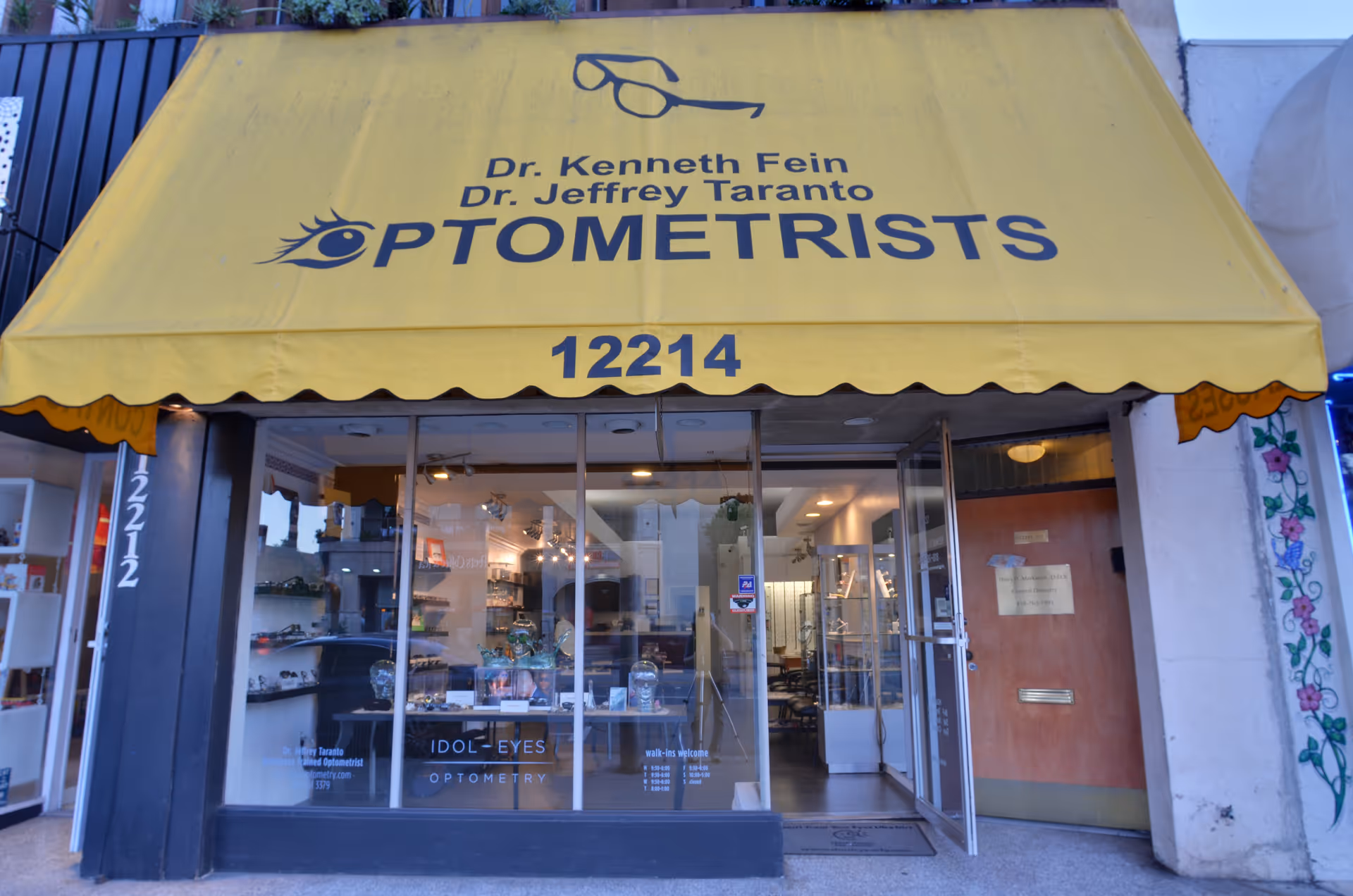 Yellow awning storefront for Opulent Eyes Optometry with glass doors and interior view.