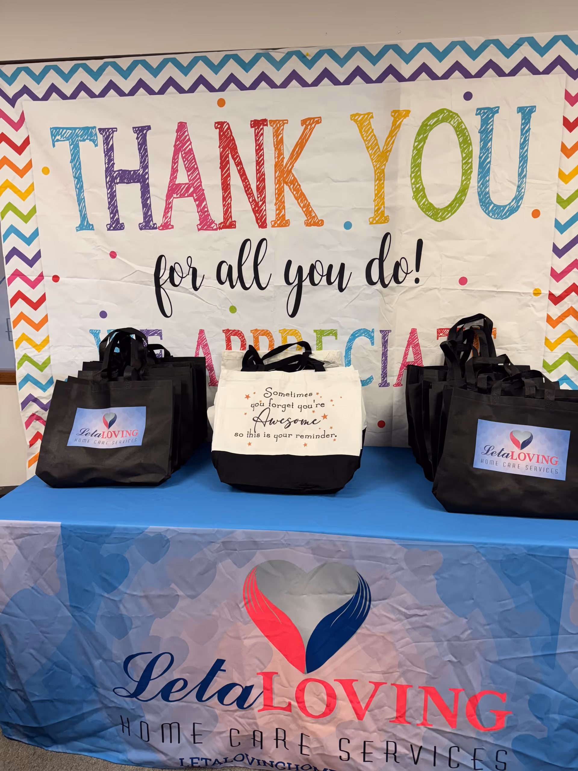 Colorful Thank You banner with black gift bags on a table at a caregiver event.