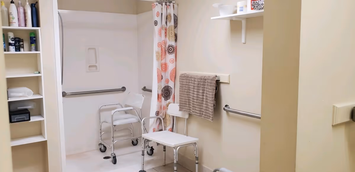 Accessible bathroom with shower chair, walker, grab bars, curtain, and shelves.