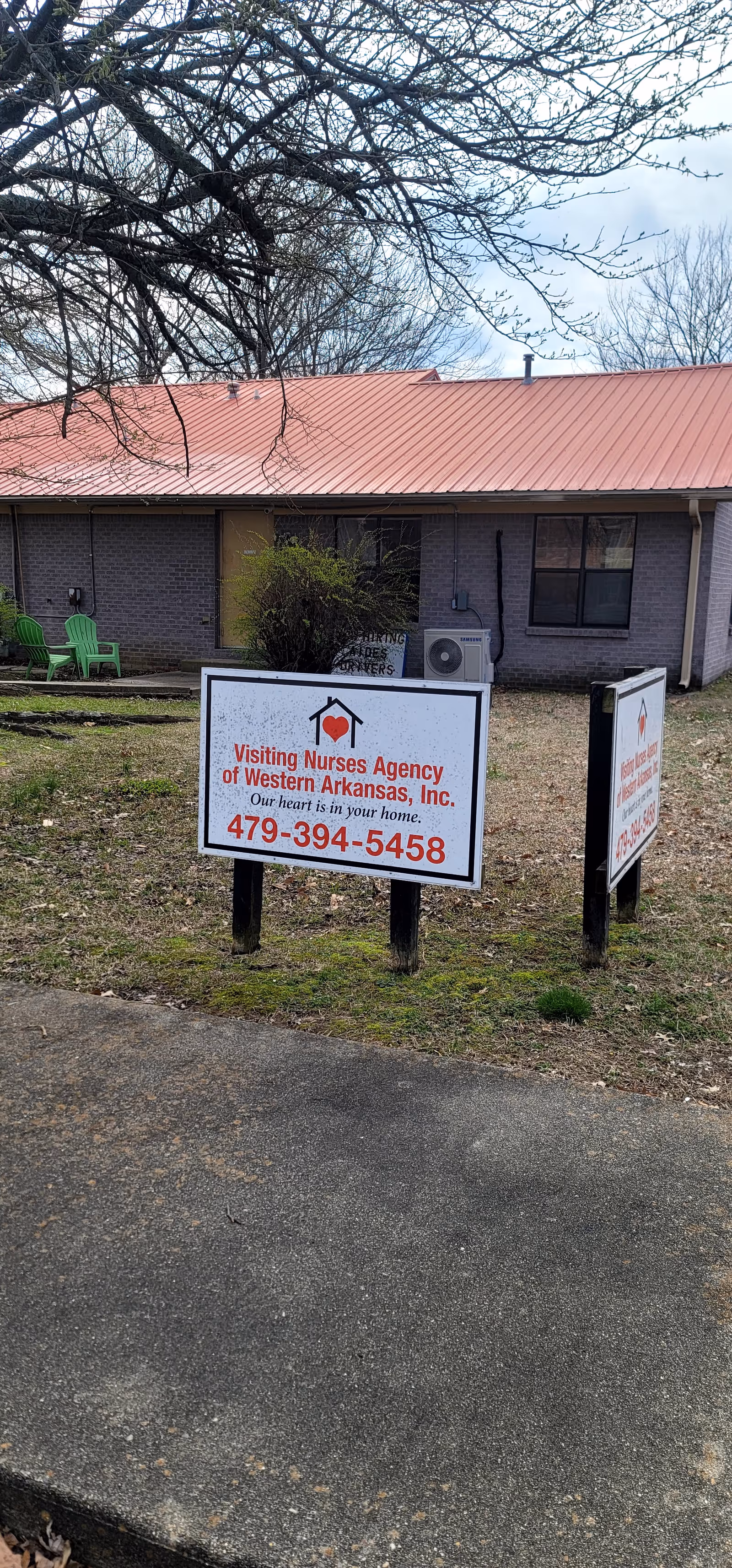 Front view of a single-story brick building with red metal roof and Visiting Nurses Agency signage.