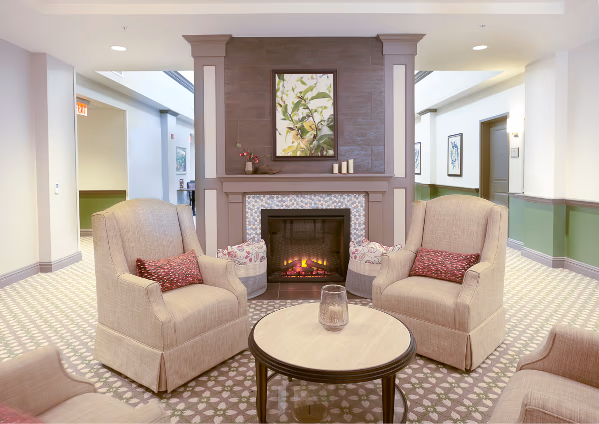 Cozy lounge with beige armchairs around a circular coffee table by a lit fireplace