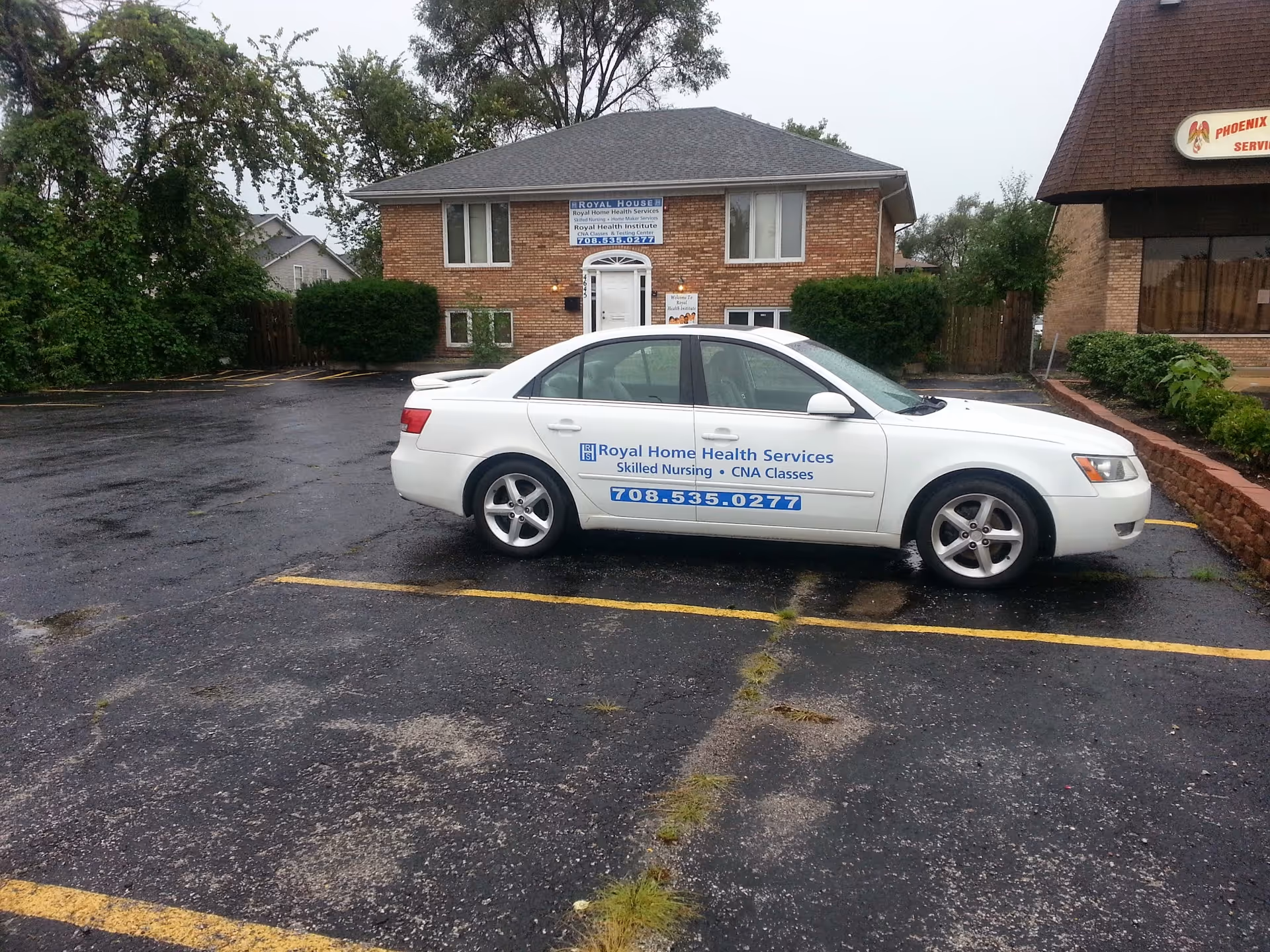 White sedan with Royal Home Health Services logo parked in front of brick senior housing facility.