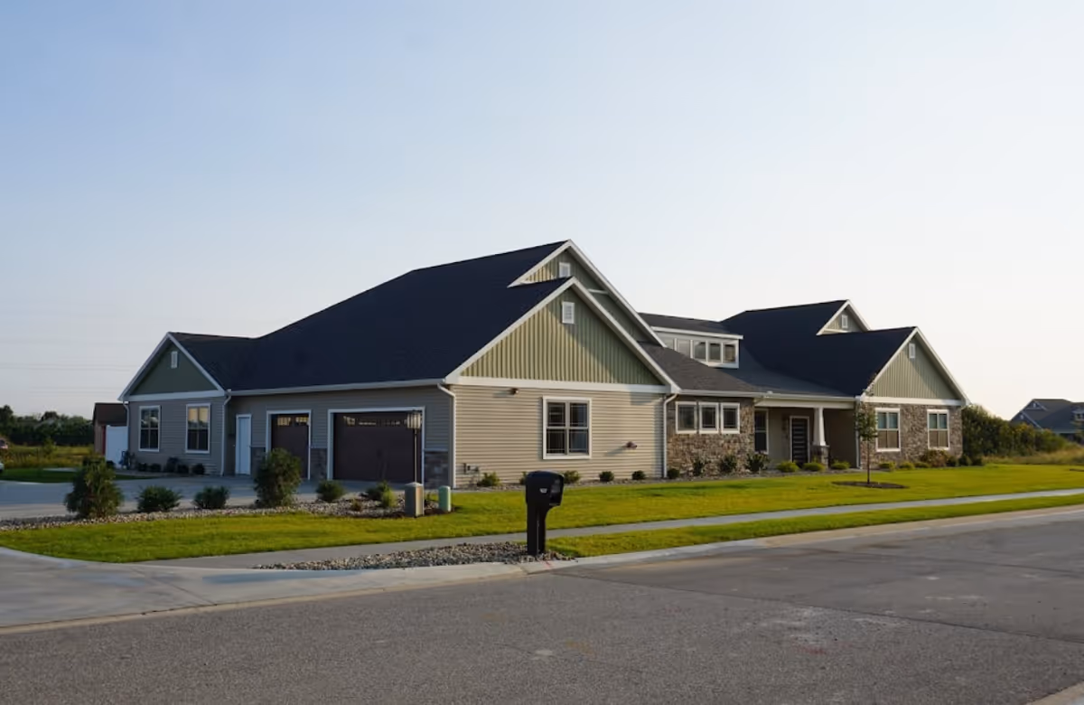 Front exterior view of a multi-gabled senior living facility with a manicured lawn.