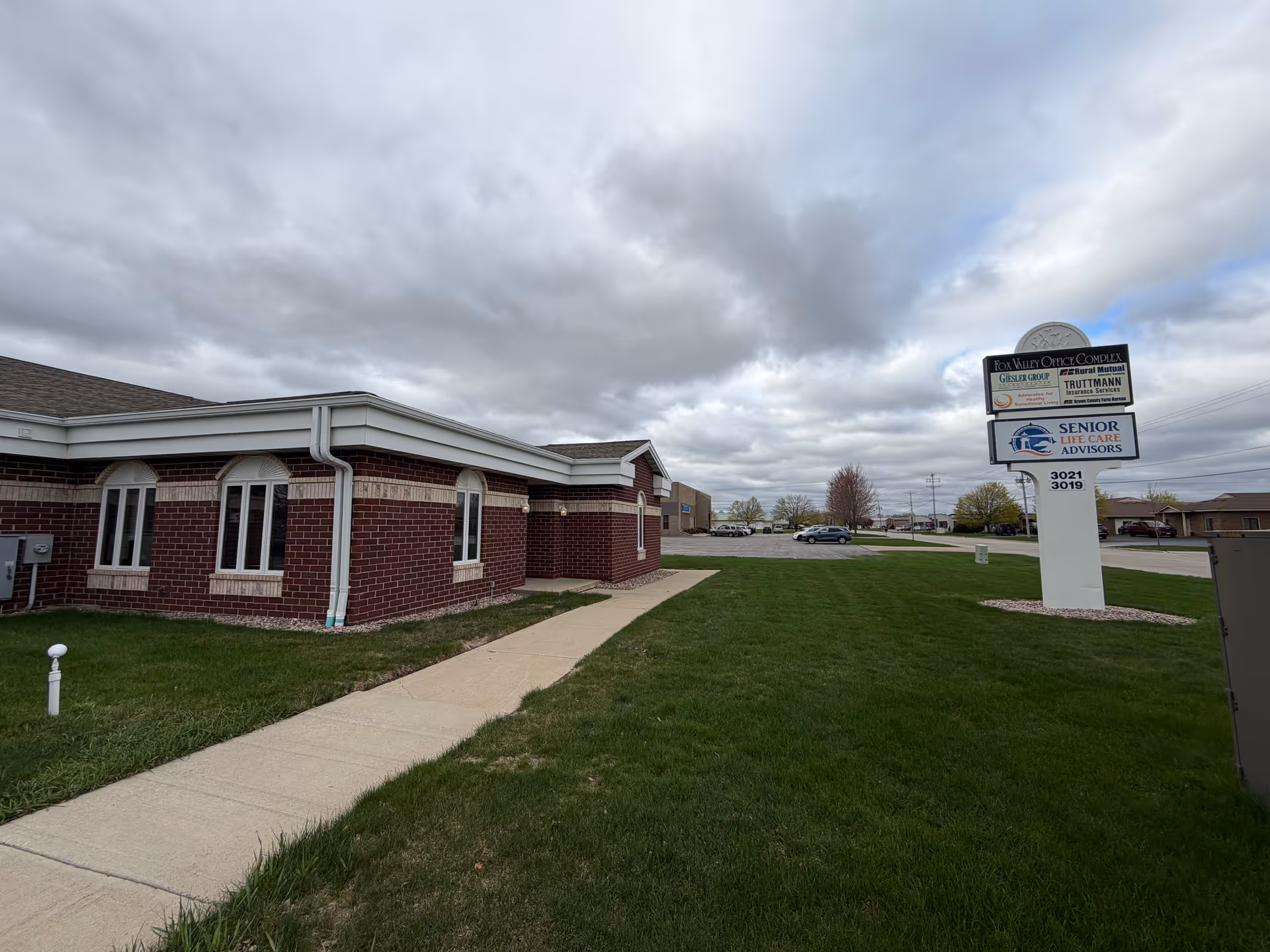 Brick senior living facility building with a sidewalk, green lawn, and sign in front.