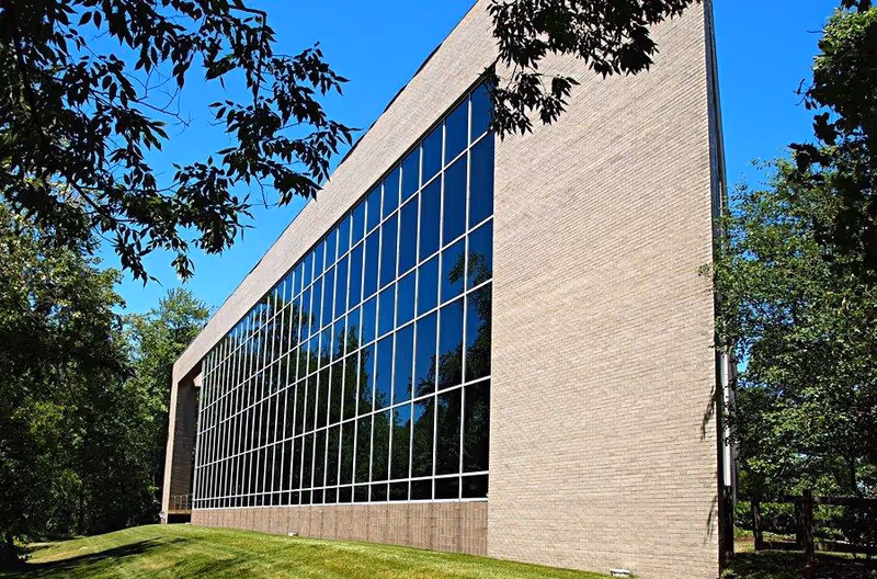 Brick building with large glass windows reflecting trees under a blue sky.