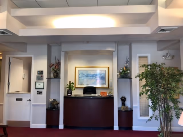 Reception desk in a senior care facility lobby, with plants, art, and decorative columns.