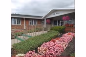 Front exterior of Conesus Lake Nursing Home with blooming pink flowers along the walkway.