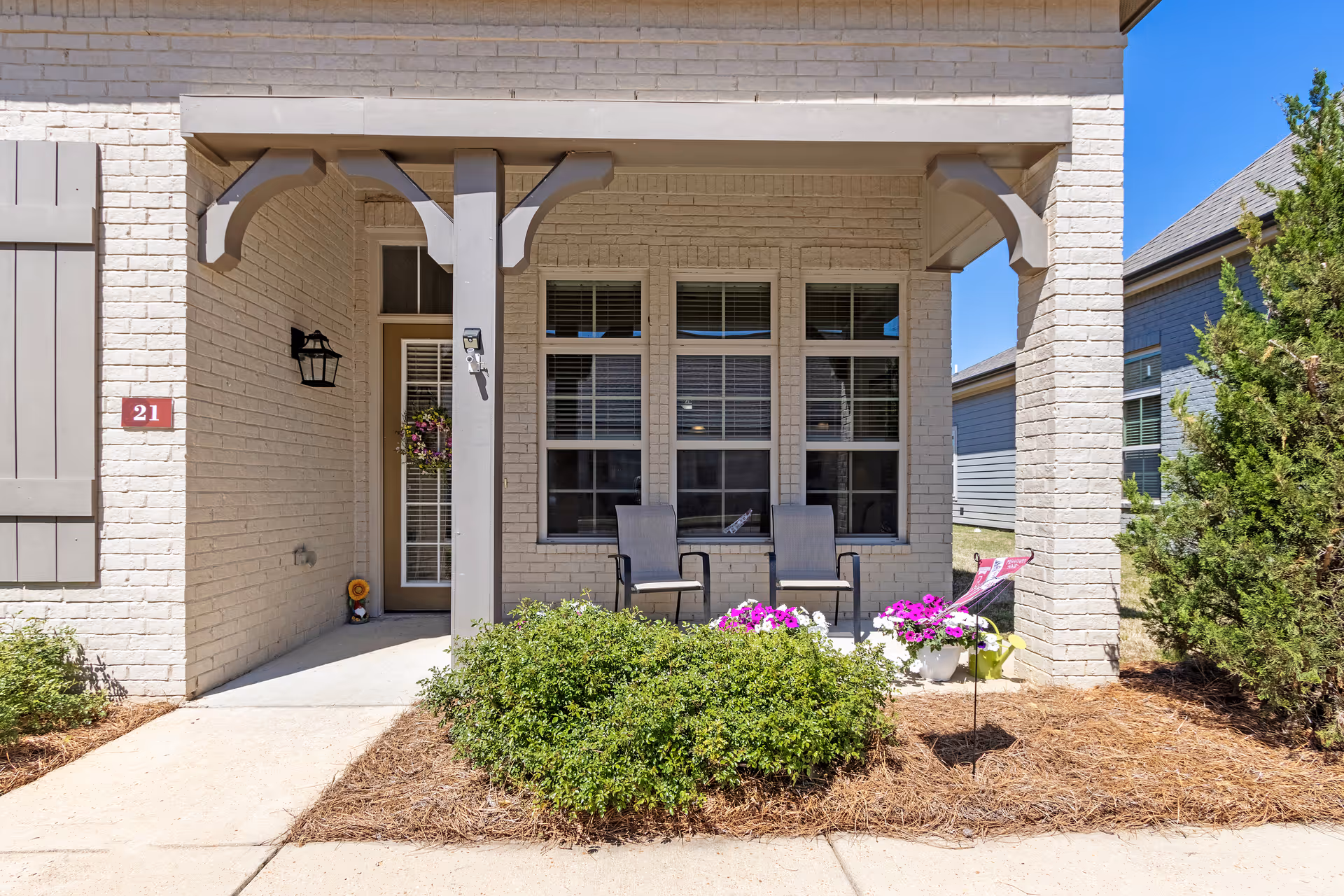 Front exterior of a brick senior living entrance with two chairs and plants.