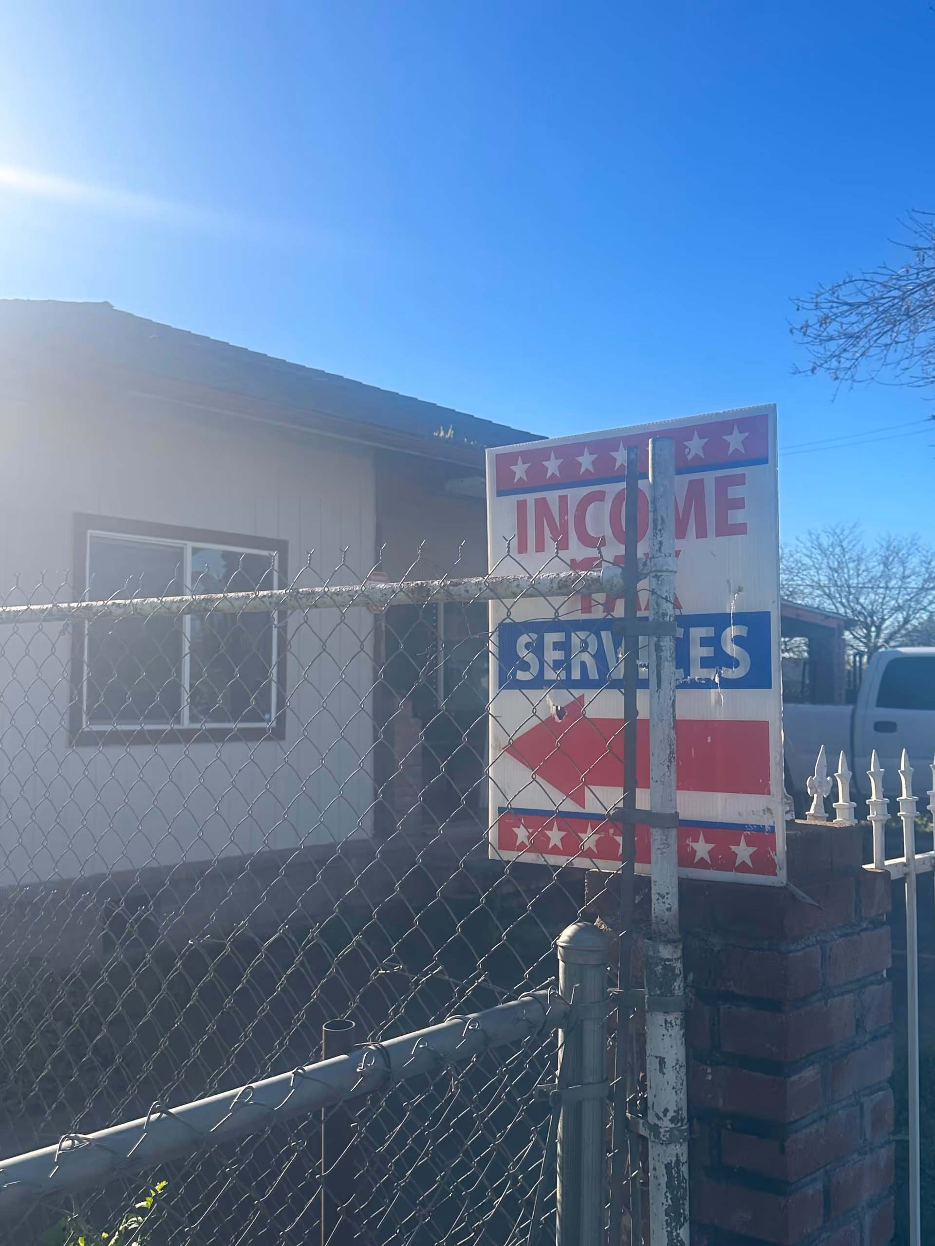 Front exterior of a small building with a chain-link fence and patriotic sign.