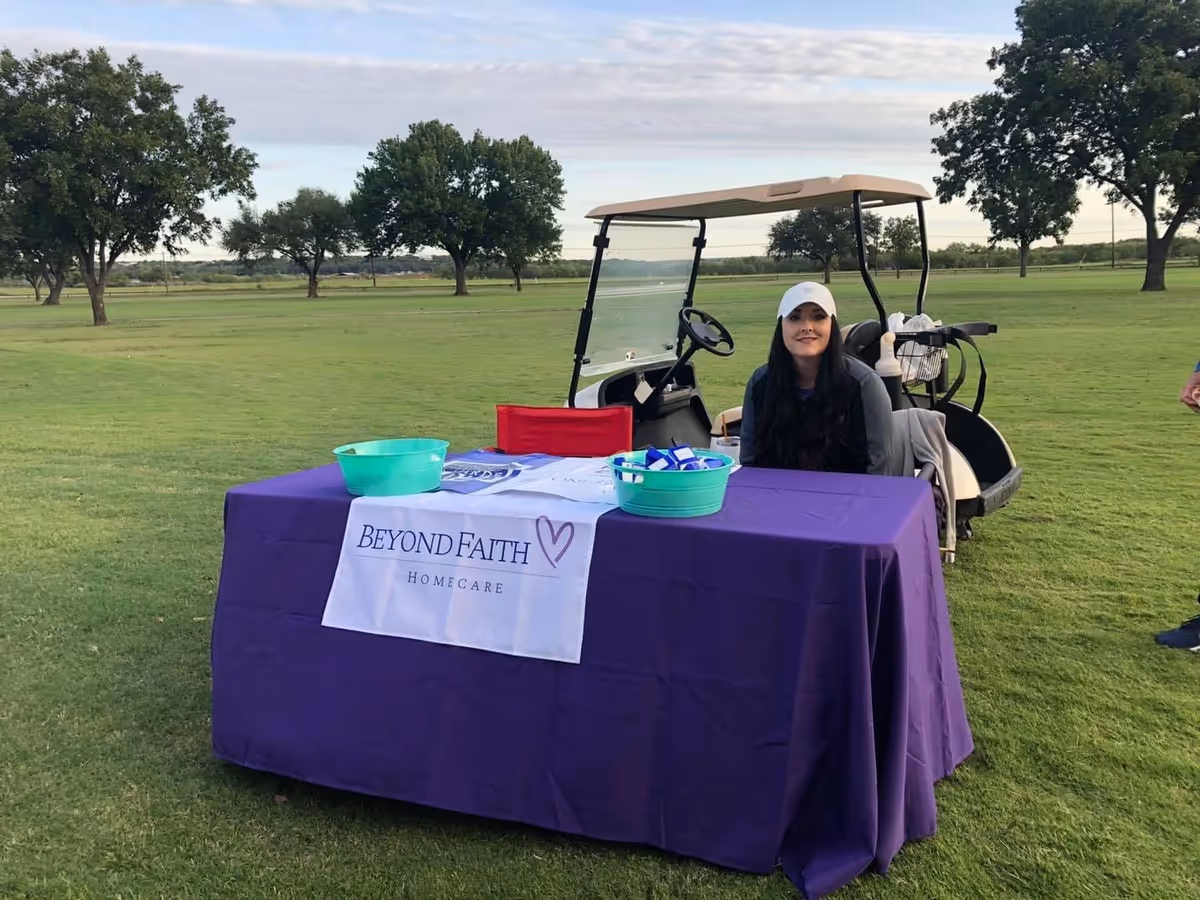 Outdoor grassy field with a purple table, banner, and a staff member beside a golf cart.