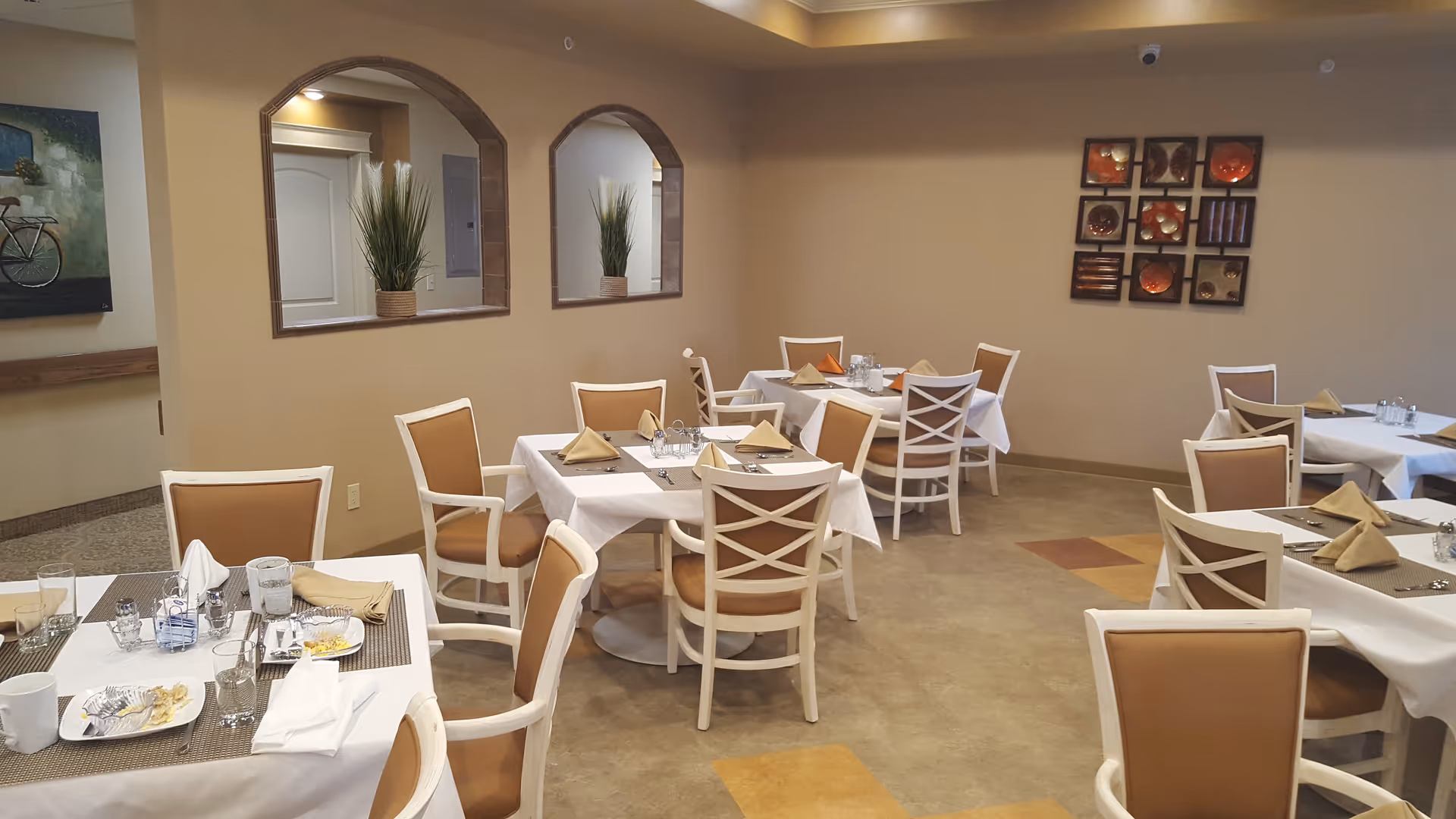 Dining room with white tablecloth tables, tan chairs, and wall art.