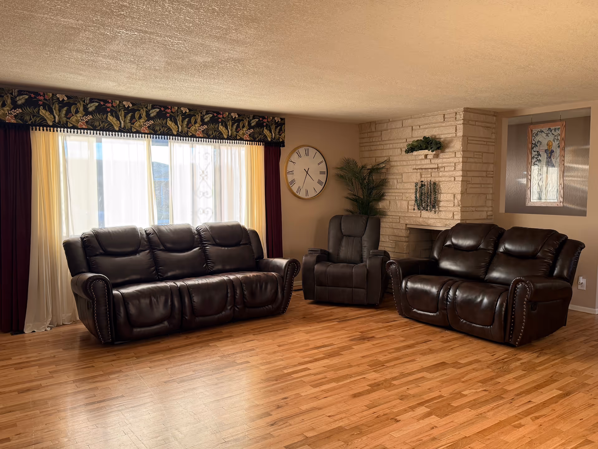 Living room with brown leather sofas, large window, clock, and brick fireplace.
