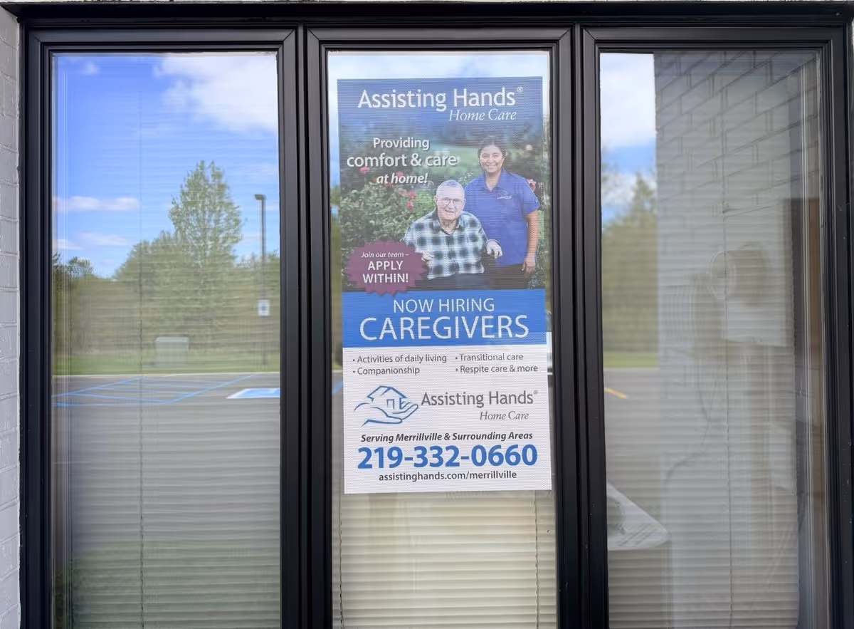 Glass storefront door with a poster advertising caregiver jobs for Assisting Hands Merrillville.