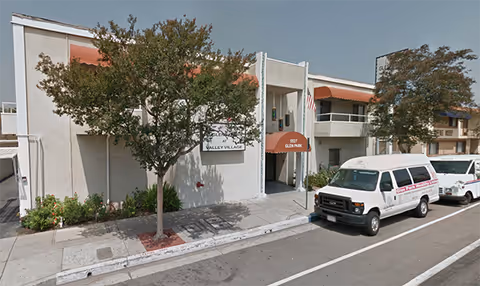 Exterior view of Glen Park at Valley Village building along a sidewalk with parked vans