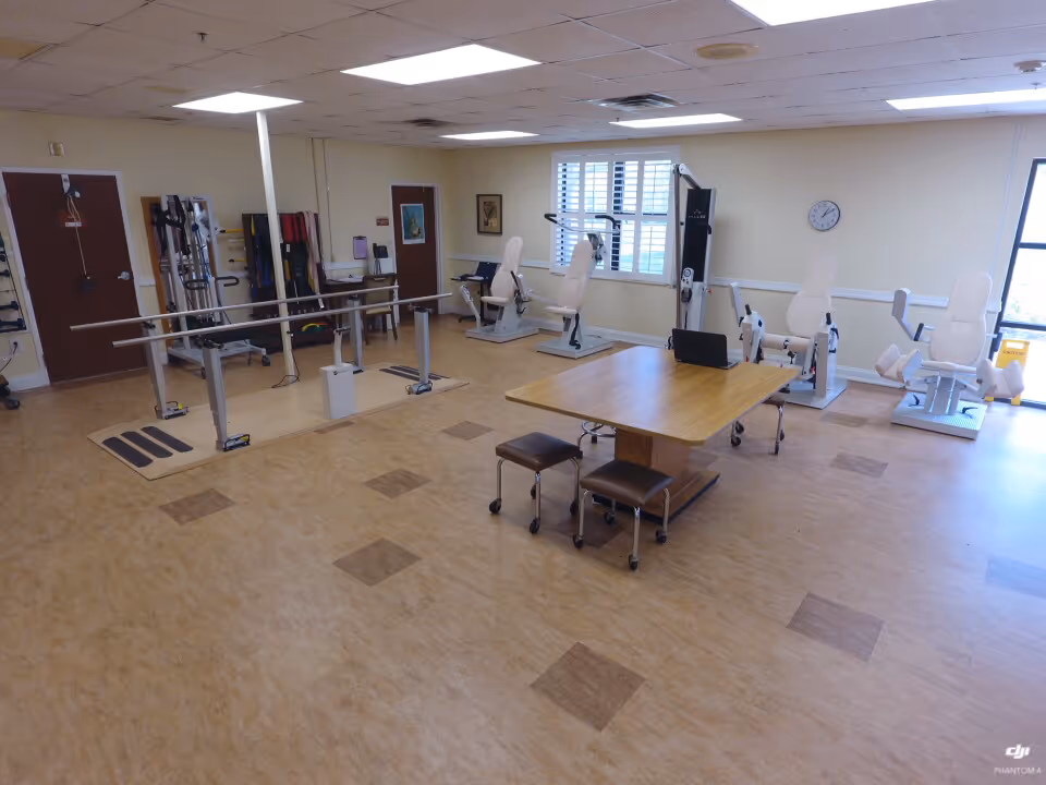 Senior living gym and therapy room with parallel bars, exercise machines, and a table in center.