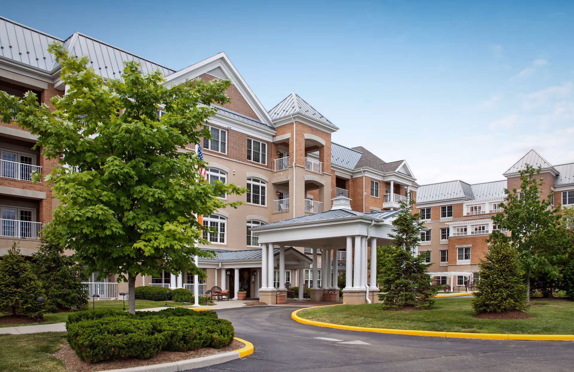 Exterior view of a senior living building with a covered entrance and landscaped grounds.