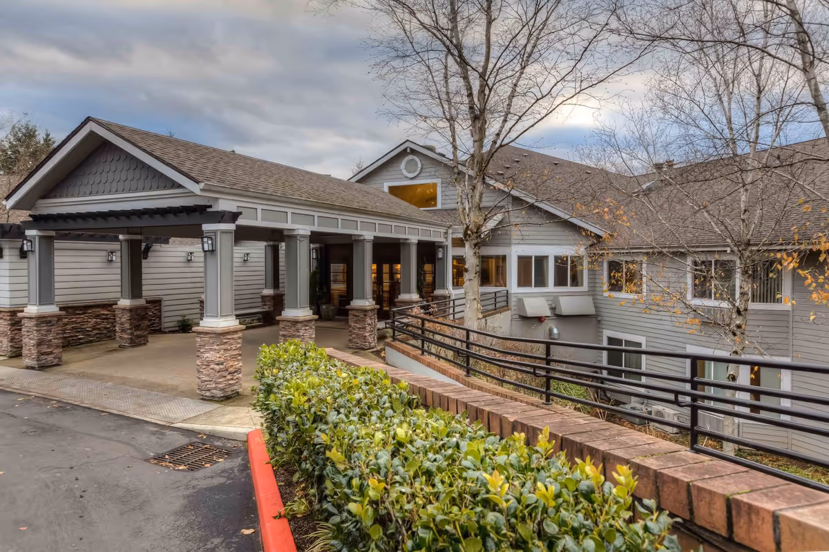 Facade of Regency Park senior living facility with covered entrance, columns, and landscaped walkway.